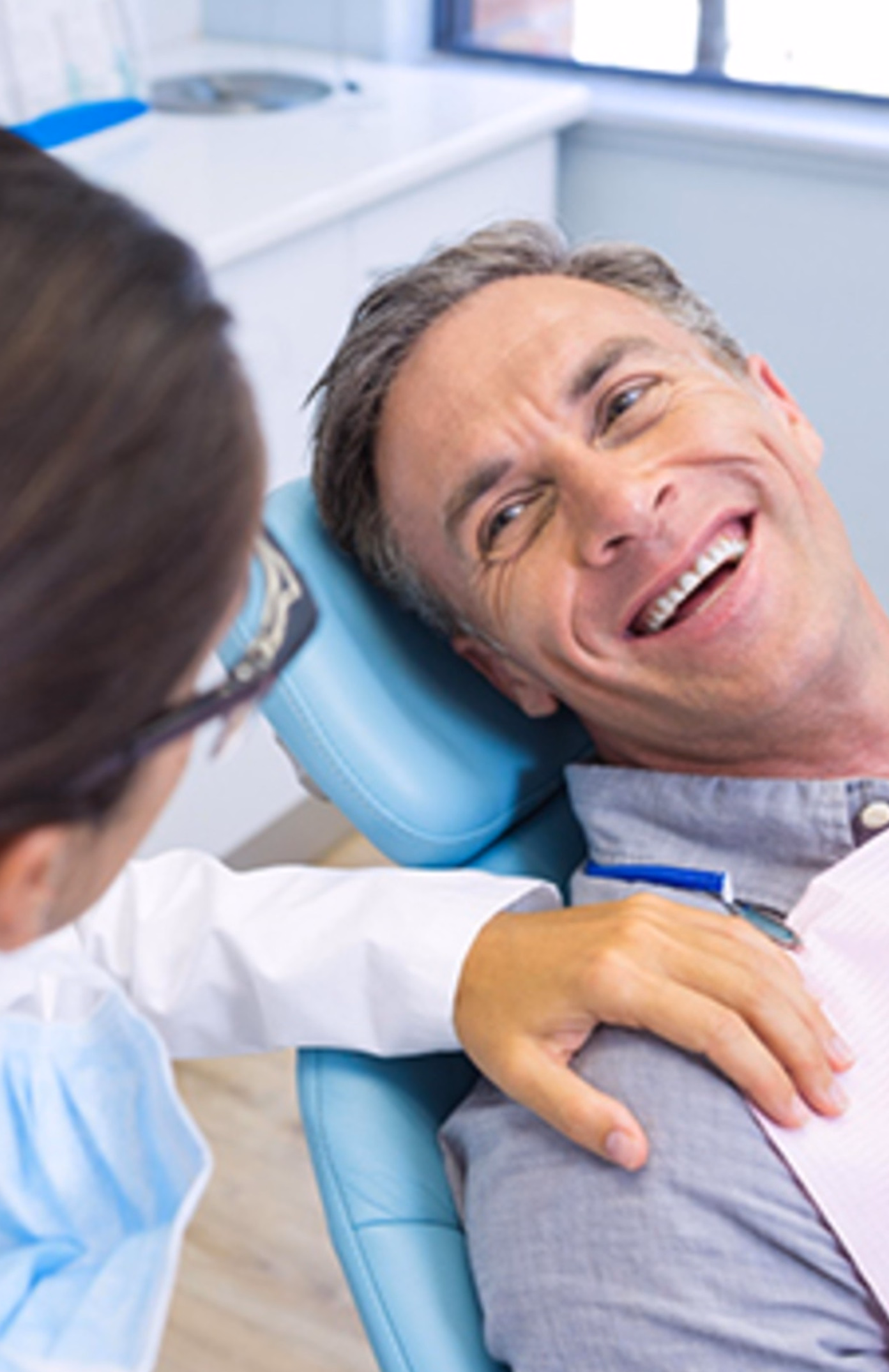 Man sitting in a dentist chair smiles warmly at a person in a white coat beside him. The setting conveys a friendly and comforting atmosphere.
