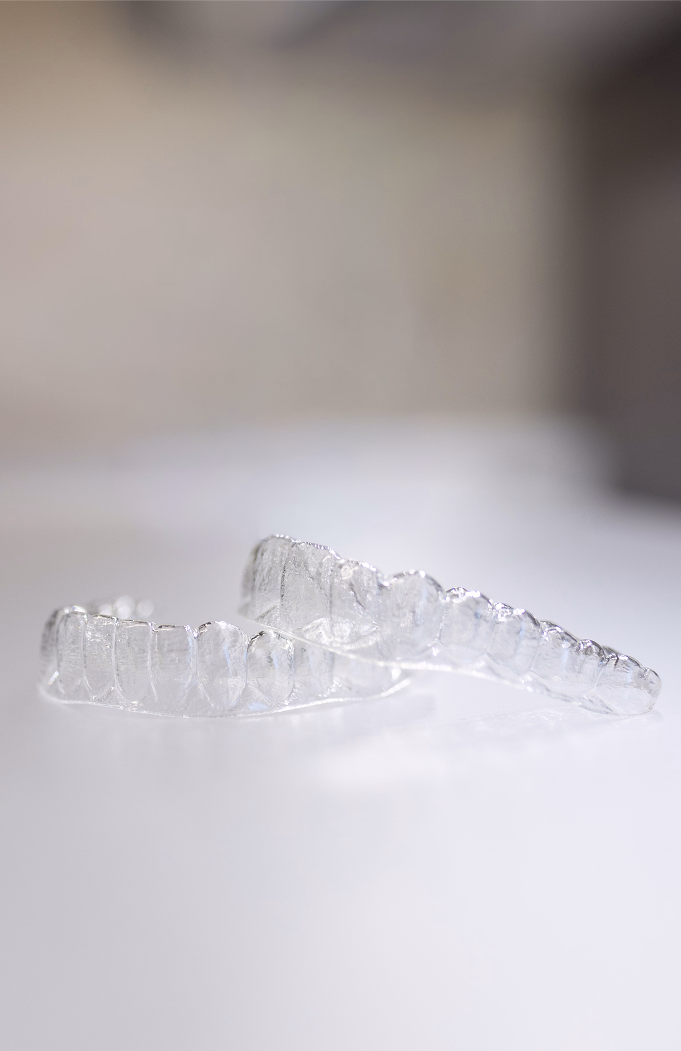 Close-up of two clear aligner trays on a white surface, with a soft-focus background. The image conveys a clean and minimalist tone related to dental care.