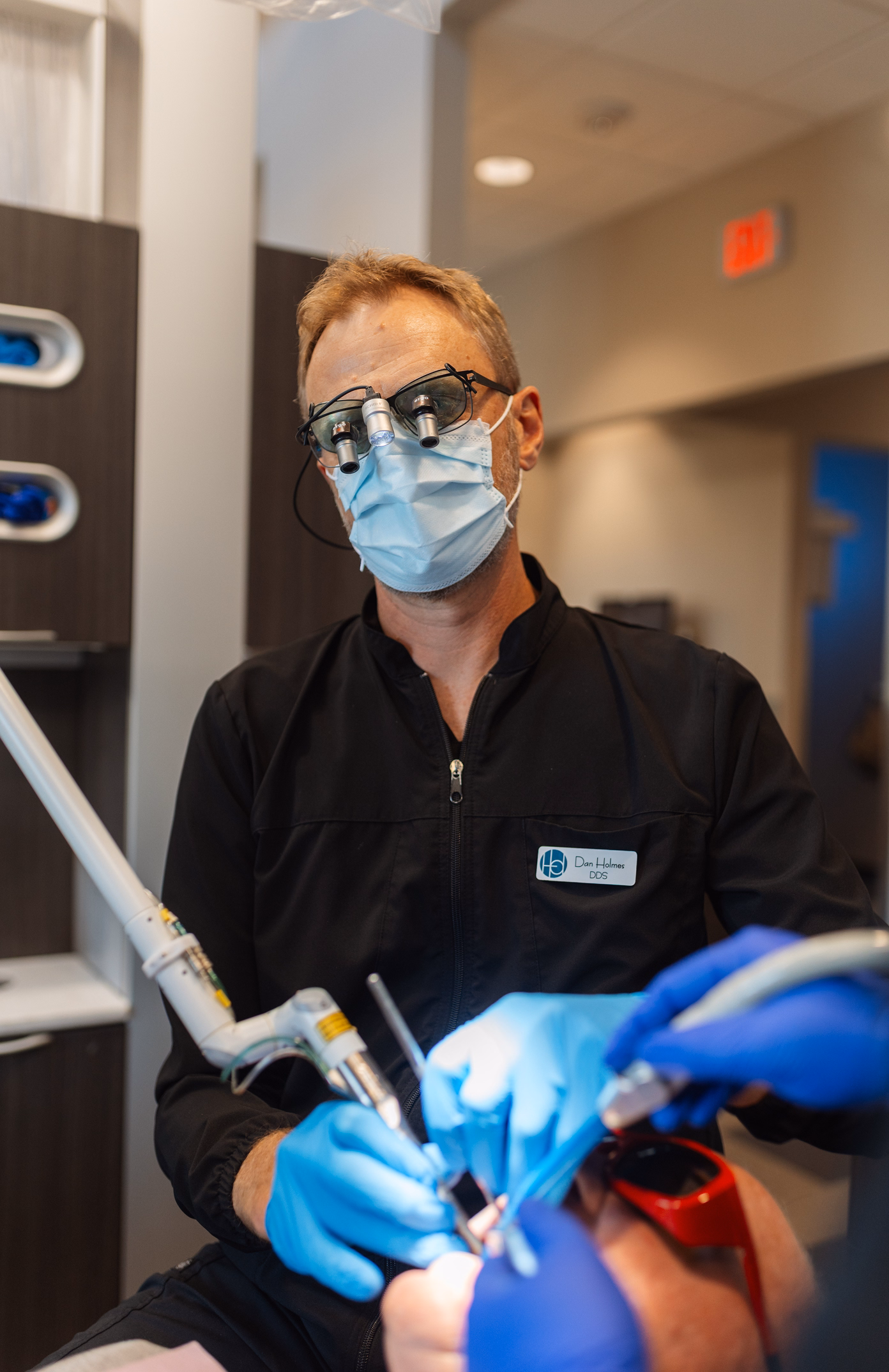 Dentist wearing magnifying glasses and a mask performs a procedure. The scene is professional, highlighting precision and care in a modern clinic setting.