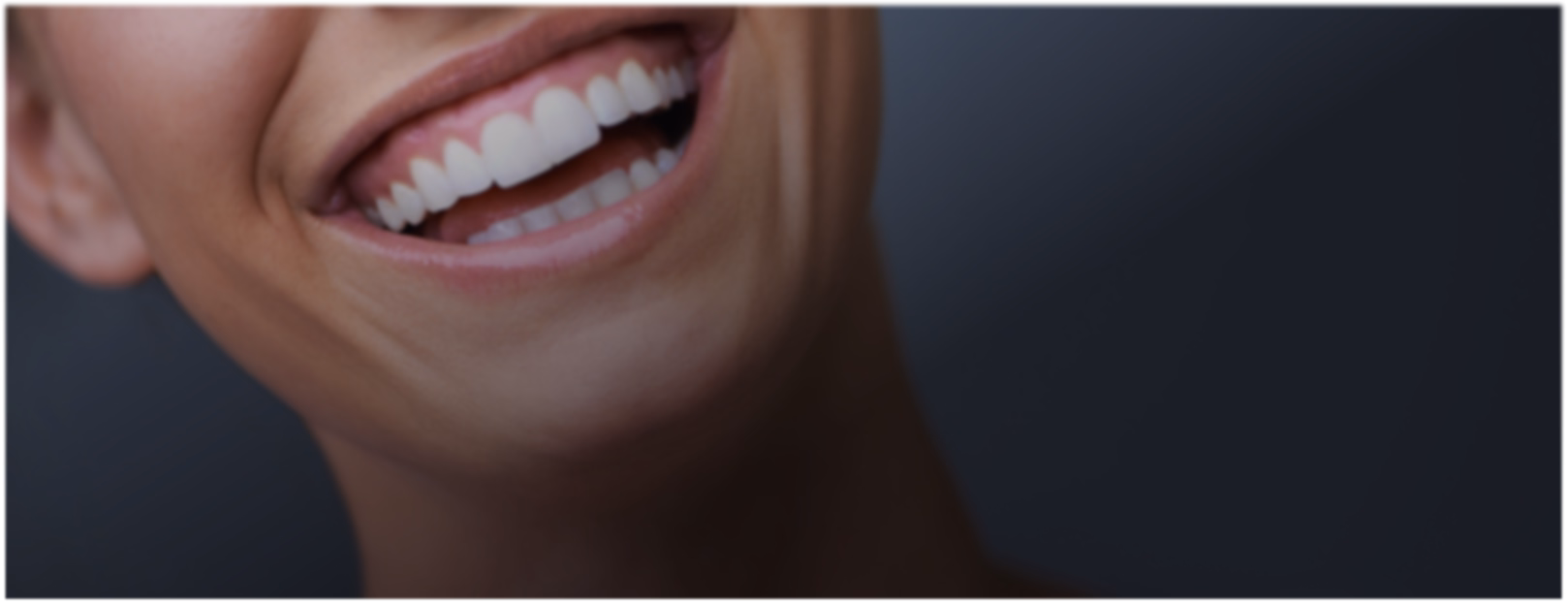 Close-up of a smiling person showing white teeth against a dark background. The image conveys happiness and warmth.